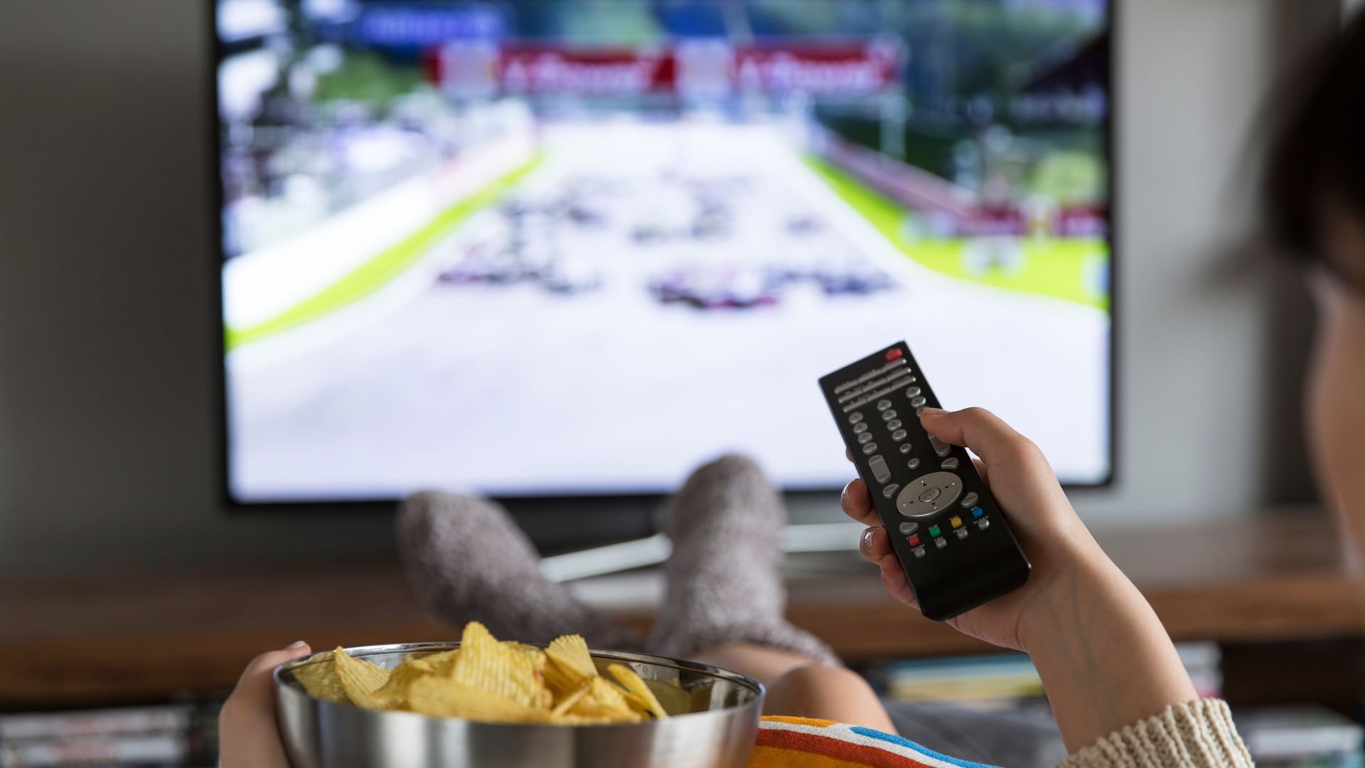 Watching sports on TV with chips, holding remote control