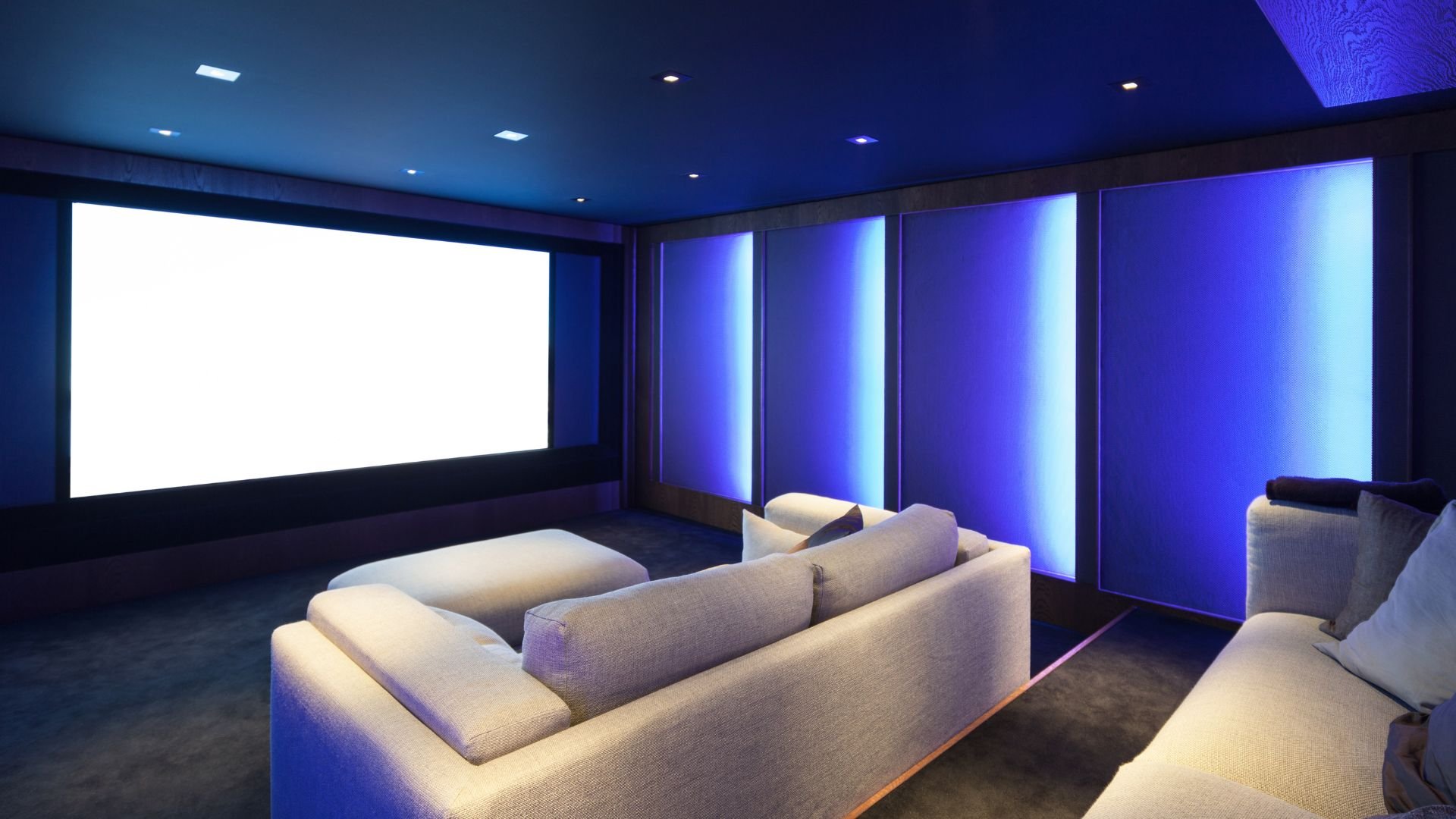 Modern home theater with white screen, blue lighting, and comfortable seating