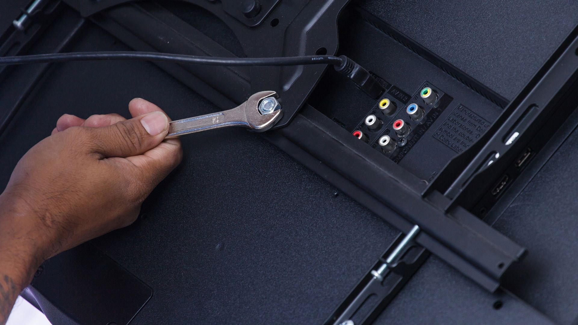 Hand using wrench near electronic device's colorful audio-video input ports