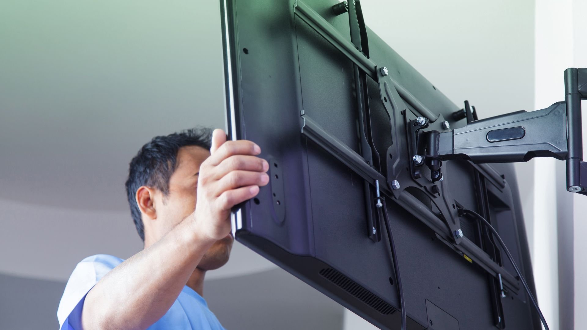 Person mounting a large display screen on a wall using a mounting arm