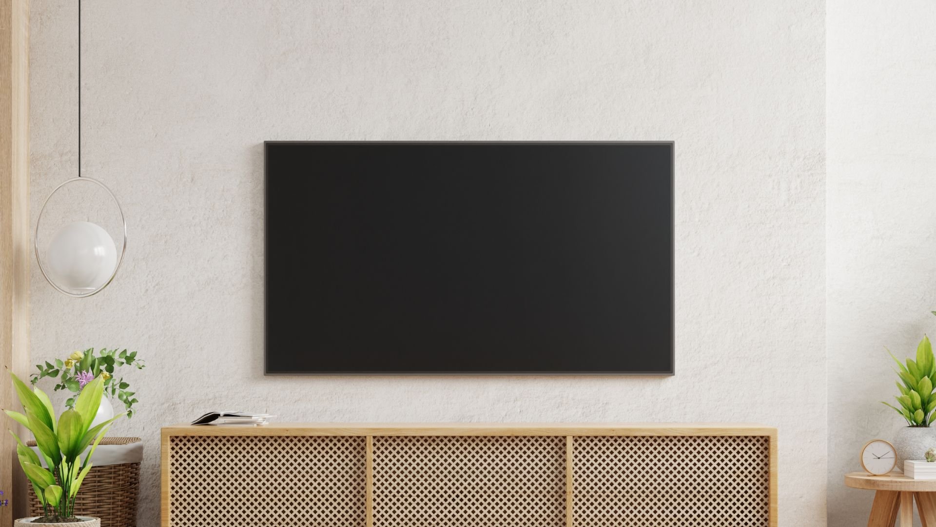 Flat screen TV mounted on white wall above wooden cabinet with plants