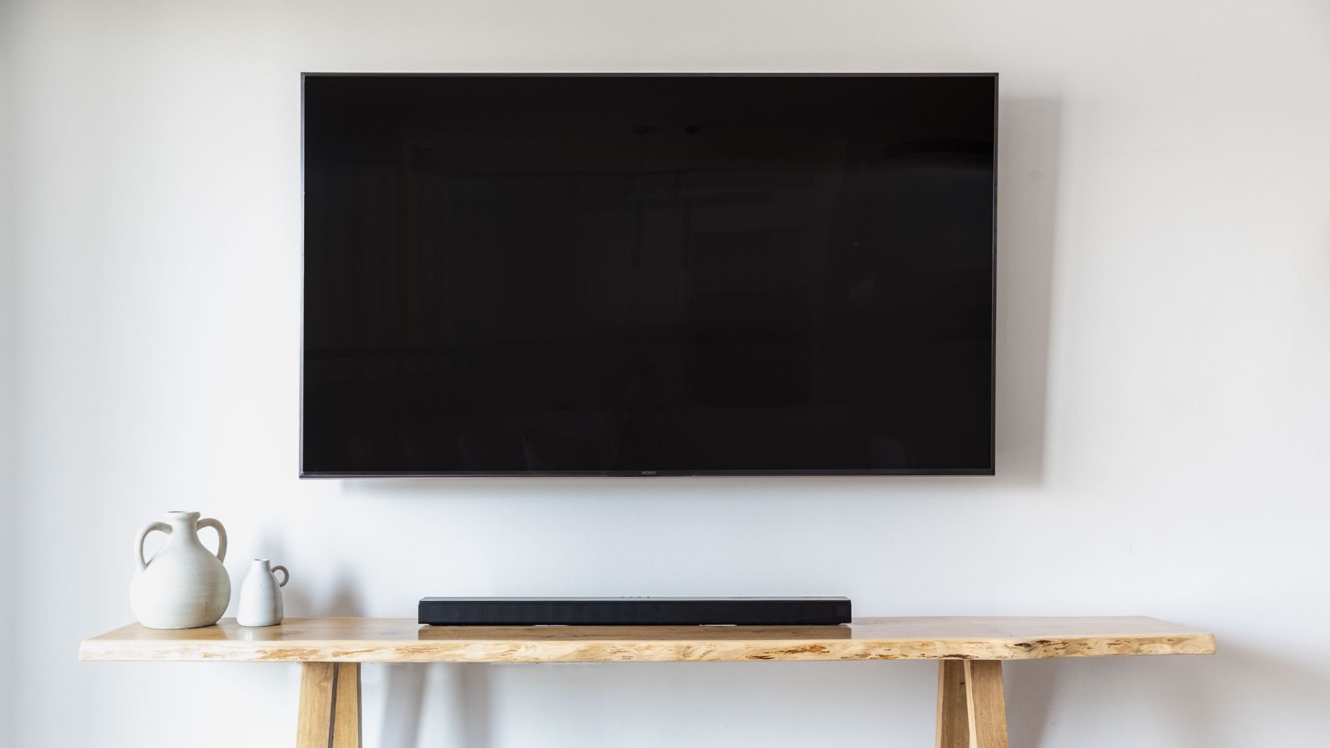 Flat screen TV mounted on white wall above wooden shelf with vases