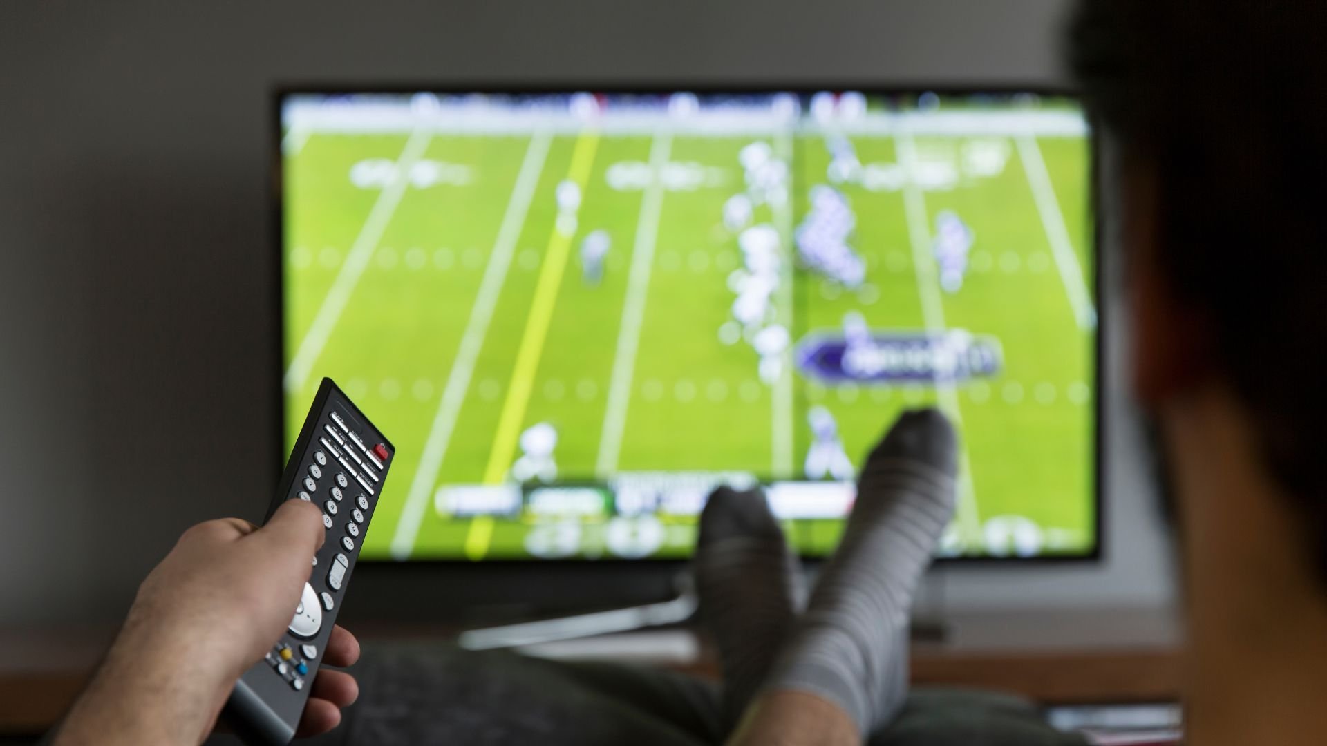 Person watching football game on TV with remote control in hand