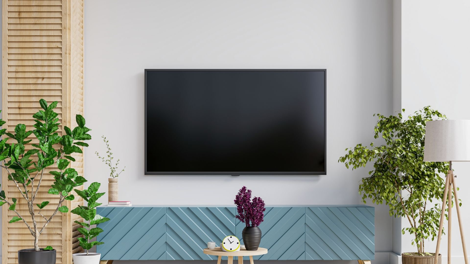 Black TV mounted on white wall with blue cabinet and decorative plants