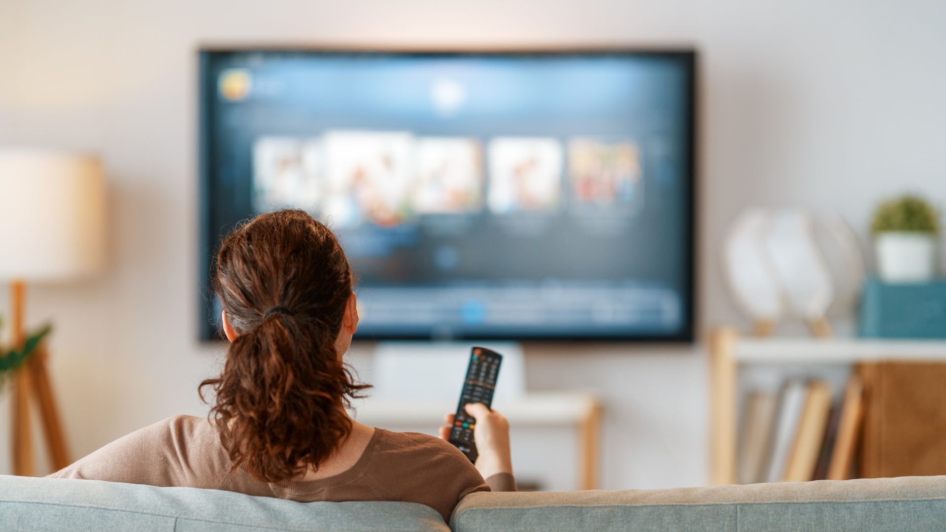 Person watching TV, holding remote control in living room