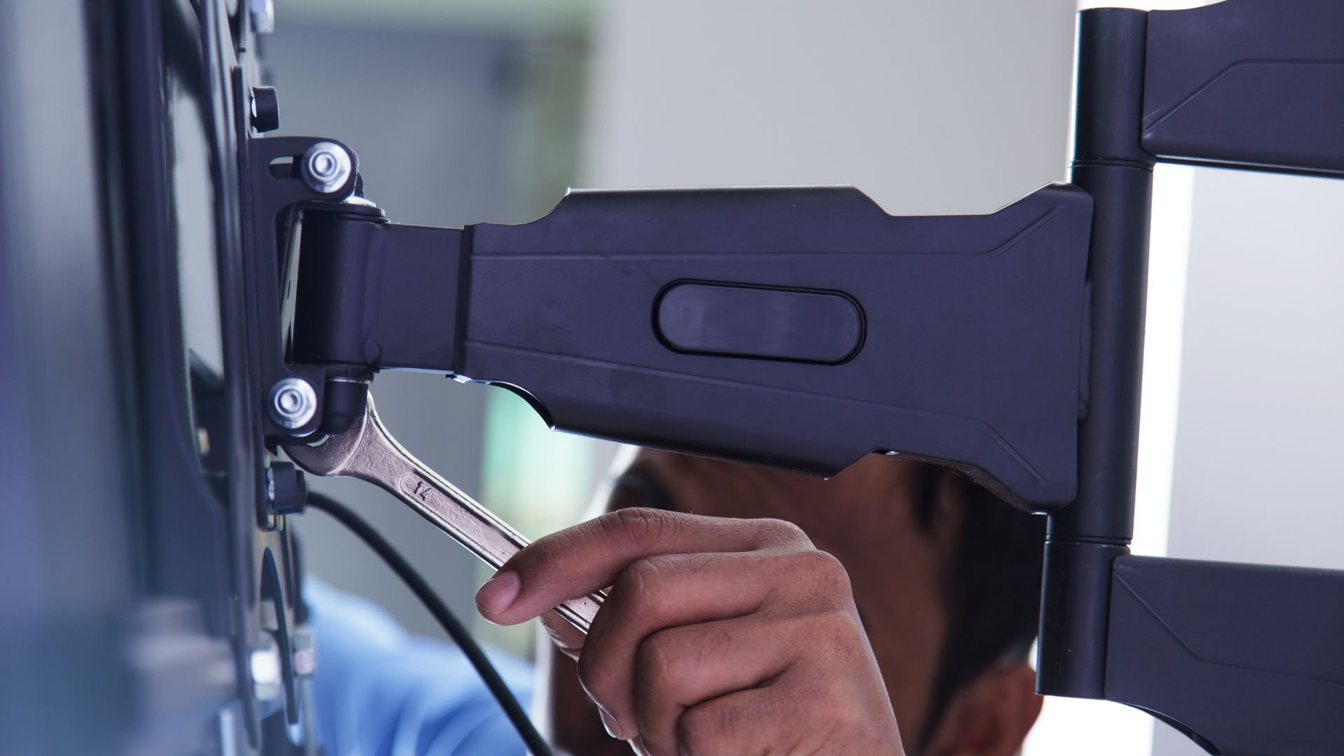 Hand adjusting monitor mount with wrench, close-up of technical installation