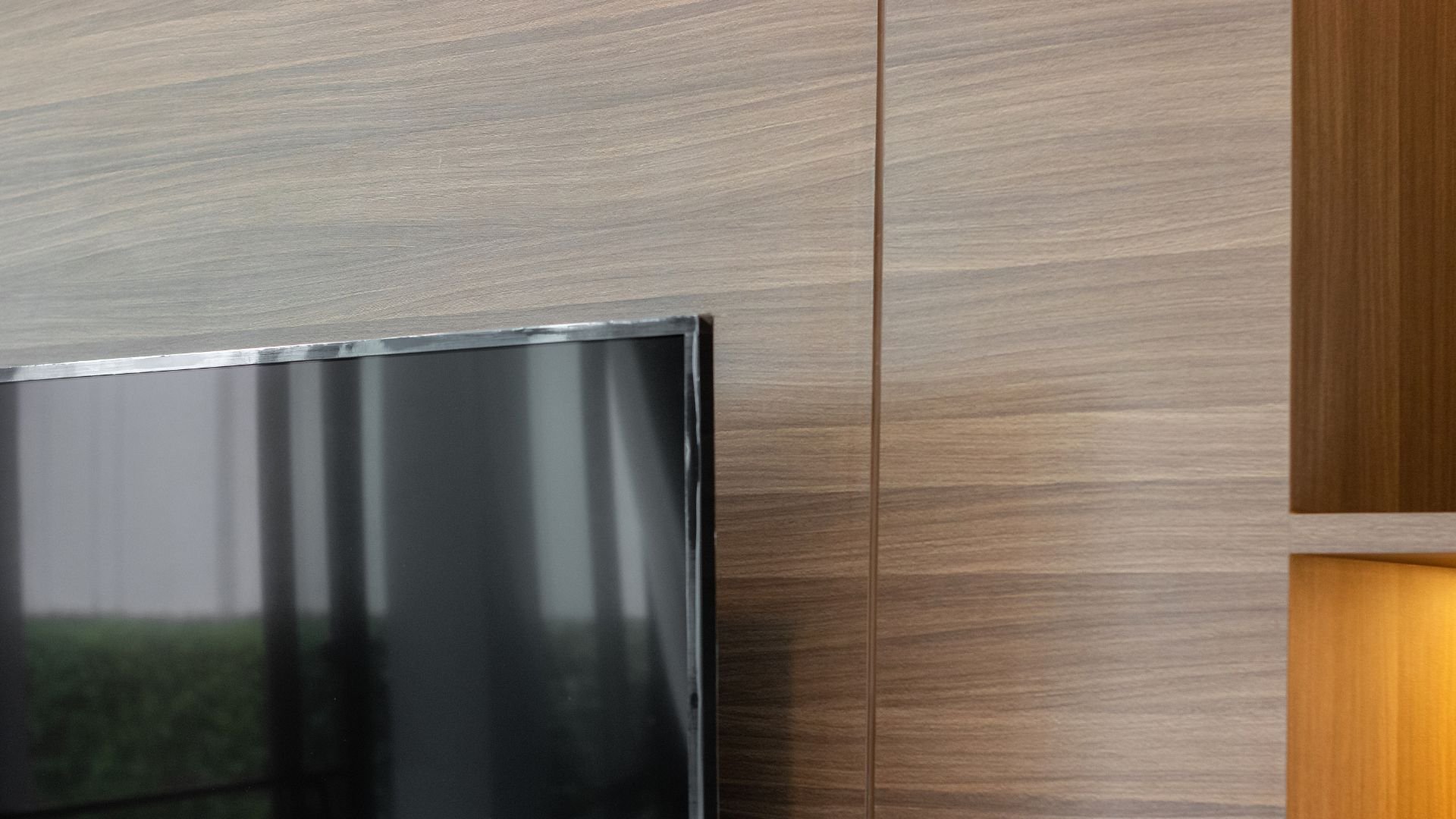 Black TV screen mounted on wooden wall with warm side lighting