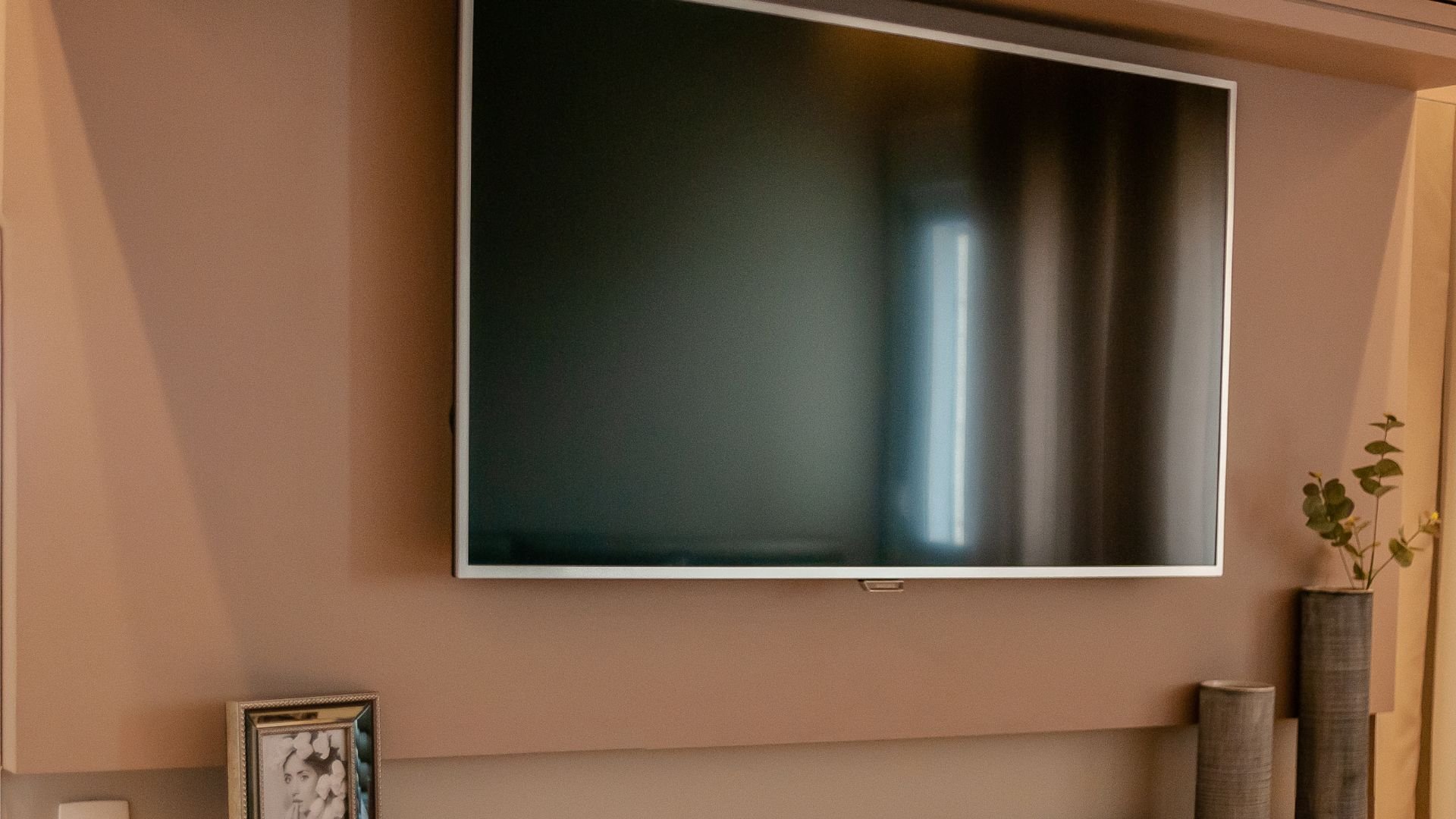 Modern flat screen TV mounted on beige wall with decorative vase